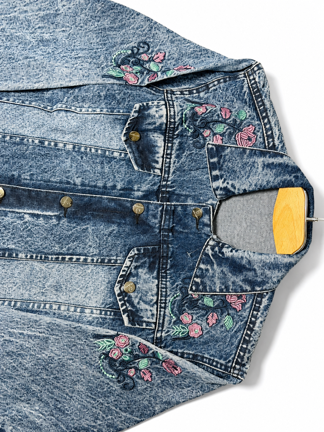 Pink floral embroidery close-up on women's acid wash denim jacket