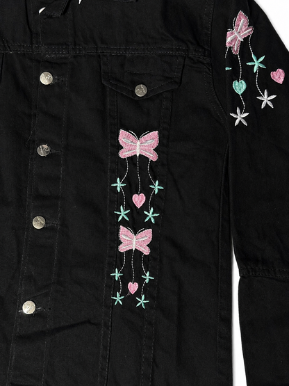 Pink bow and heart embroidery close-up on women's black denim jacket