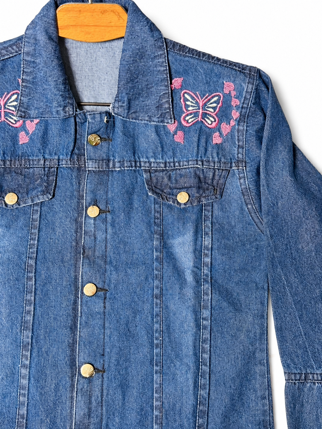 Pink butterfly and heart embroidery close-up on women's blue denim jacket
